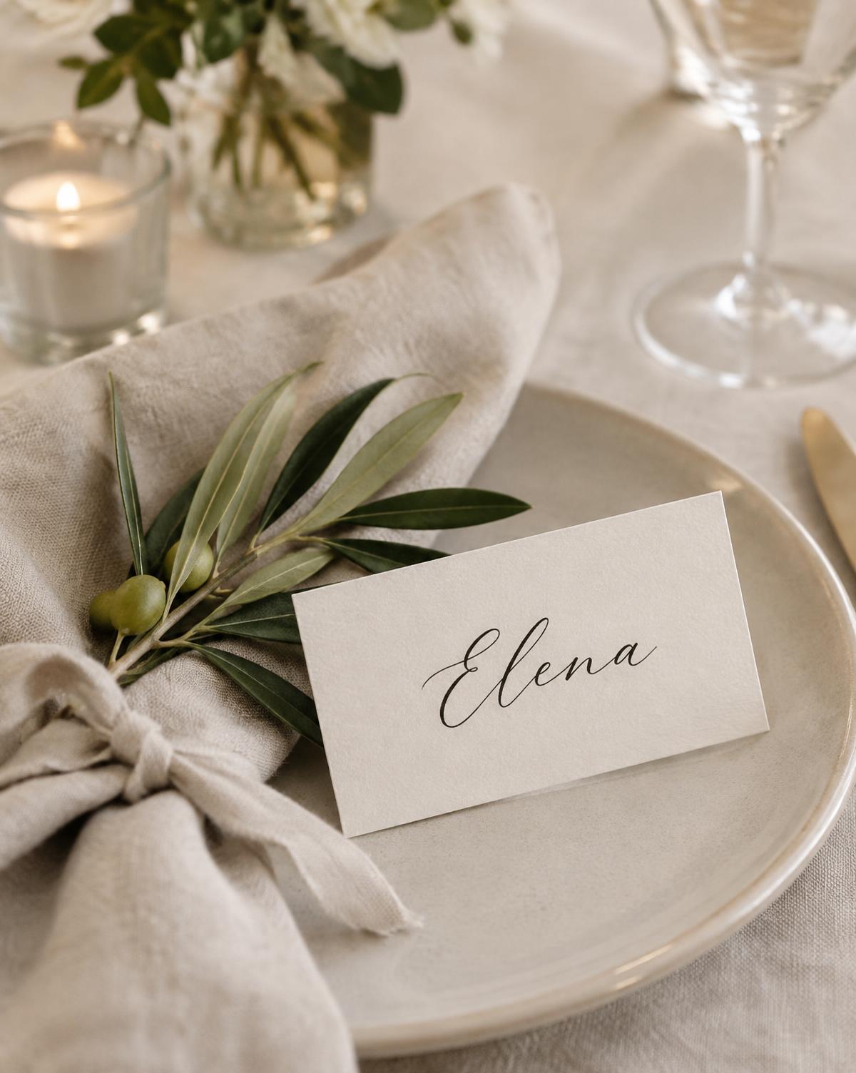 Detalle de mesa con tarjeta de caligrafía, rama de olivo y servilleta de lino